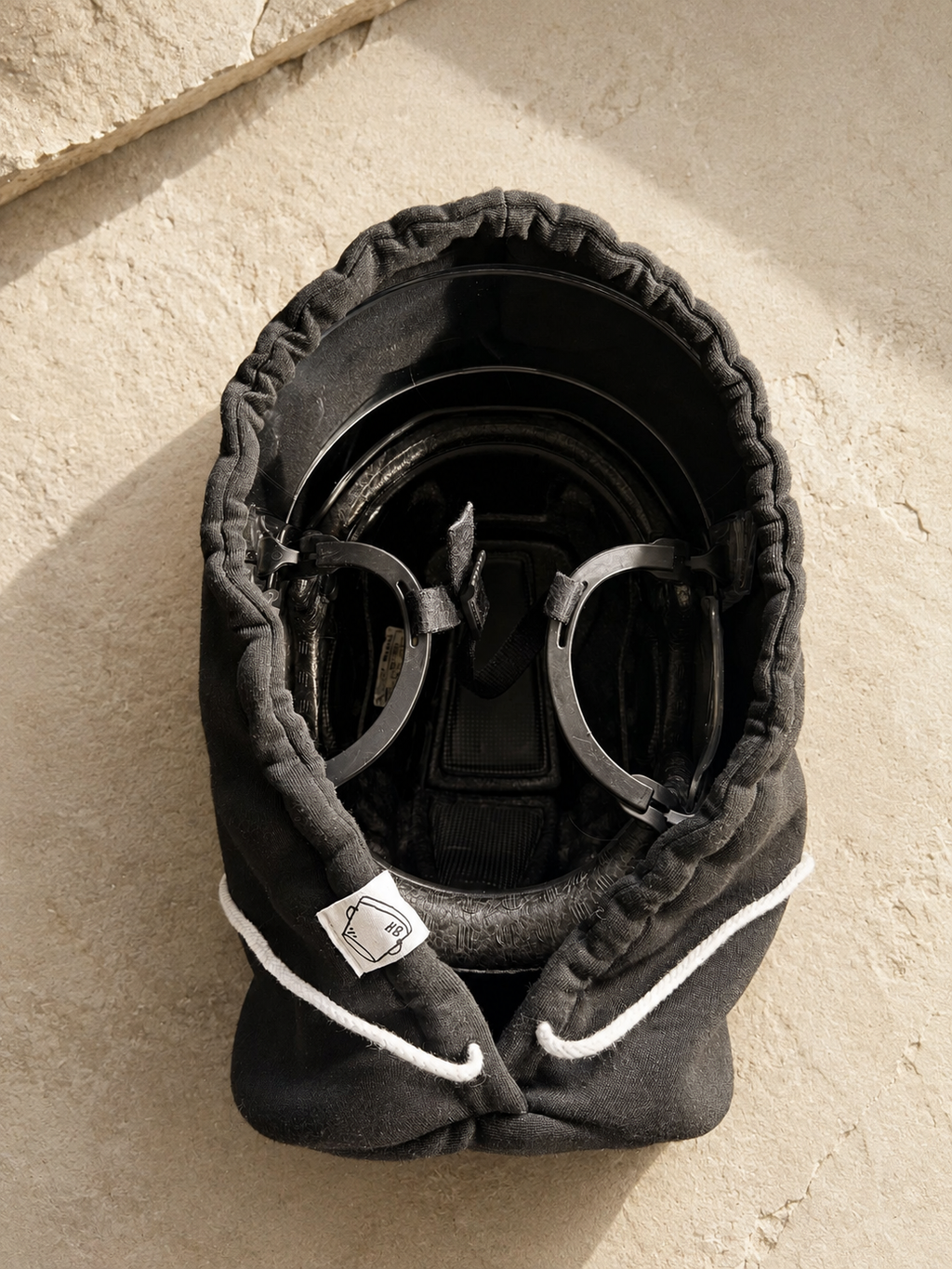 Overhead view of a black Bucket Hood covering a hockey helmet and visor with white drawstrings