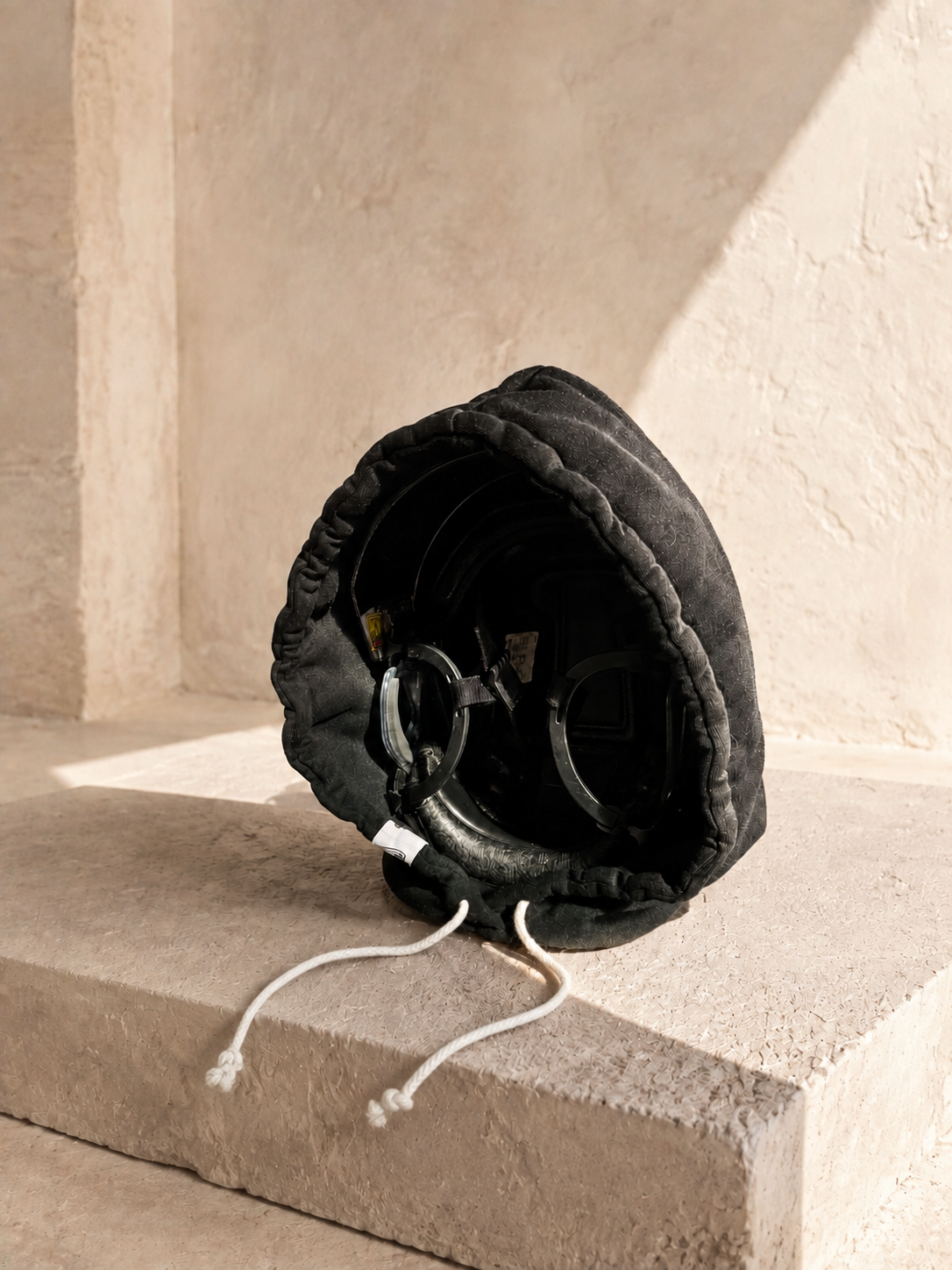 Front three-quarter view of a black Bucket Hood around a hockey helmet and visor on limestone